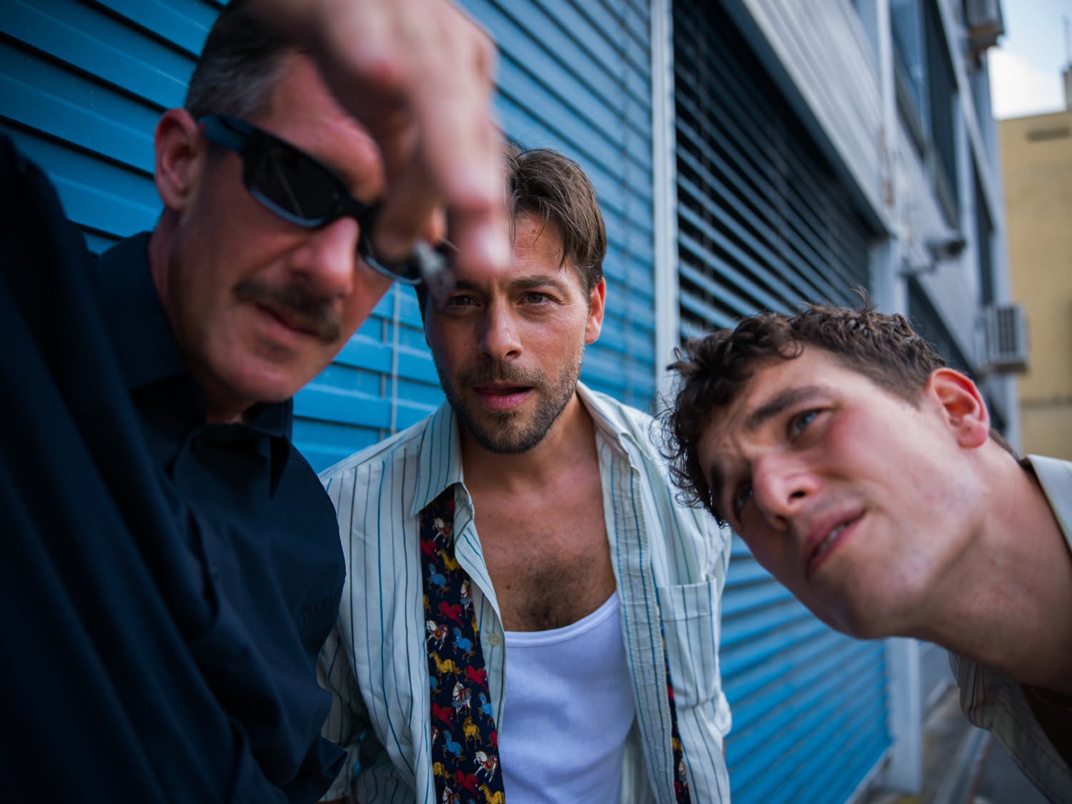 The three members of Matter leaning toward the camera beside a blue building